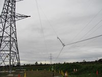 Transmission cables suspended from a metal transmission tower at a distance.