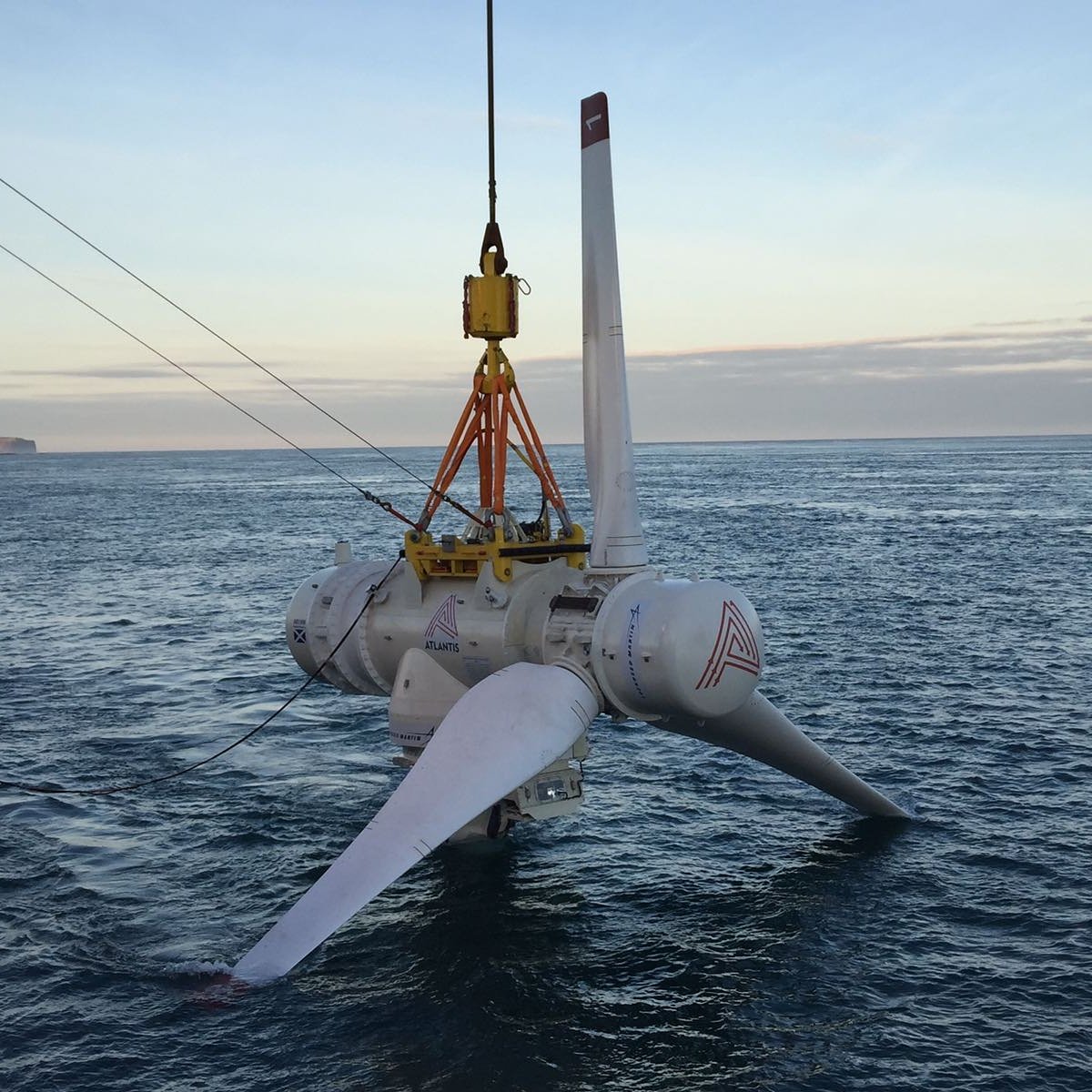 A turbine suspended just above the sea from a cable.