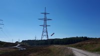 A structure being hoisted by cables up to a transmission tower.