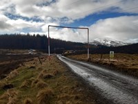 A muddy track in a rural area. An amber sign reads "Danger Overhead Live Wires" and "Maximum Working Height 5M".