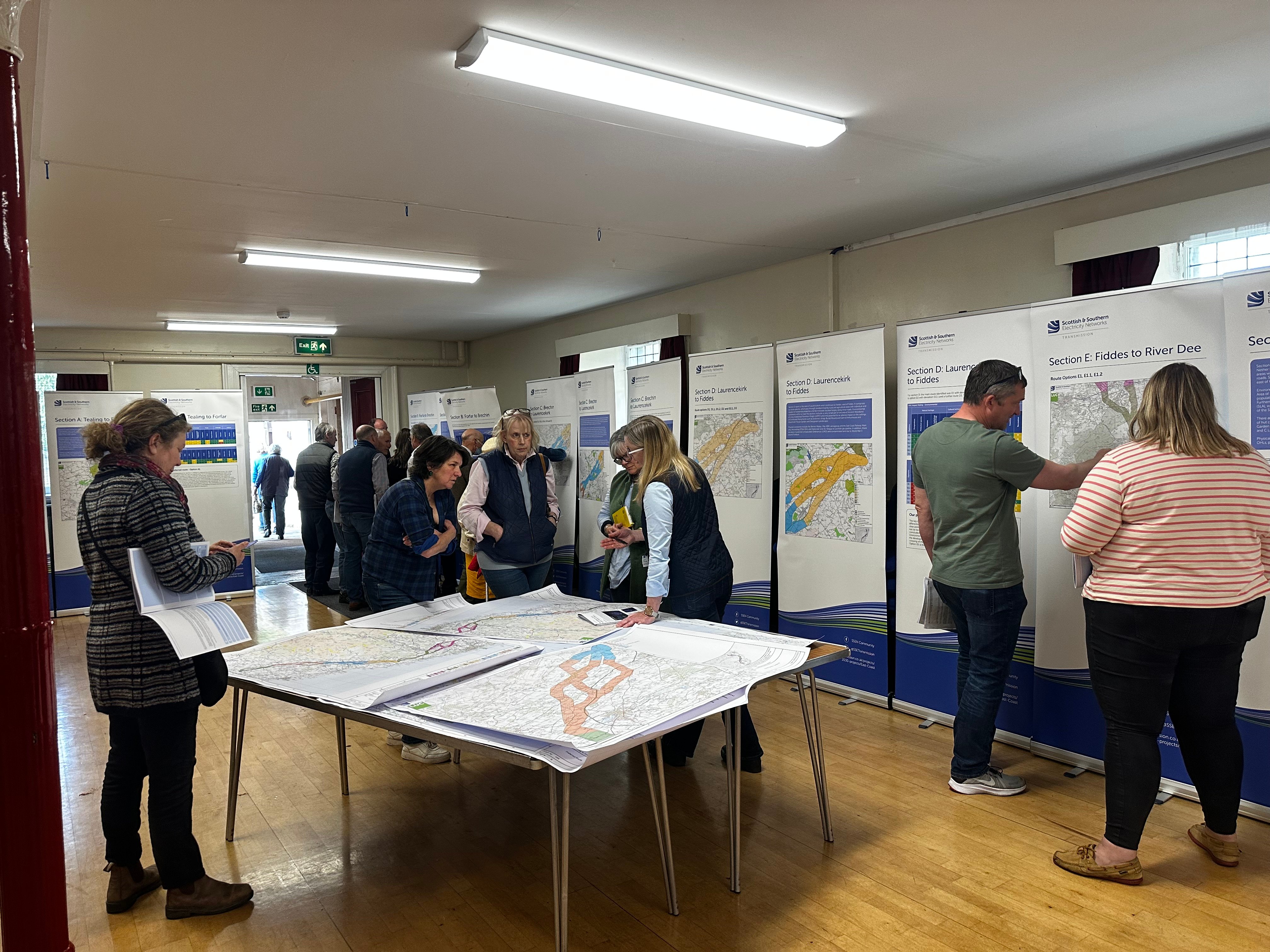 Members of the public and SSEN Transmission employees examining project posters in a hall.