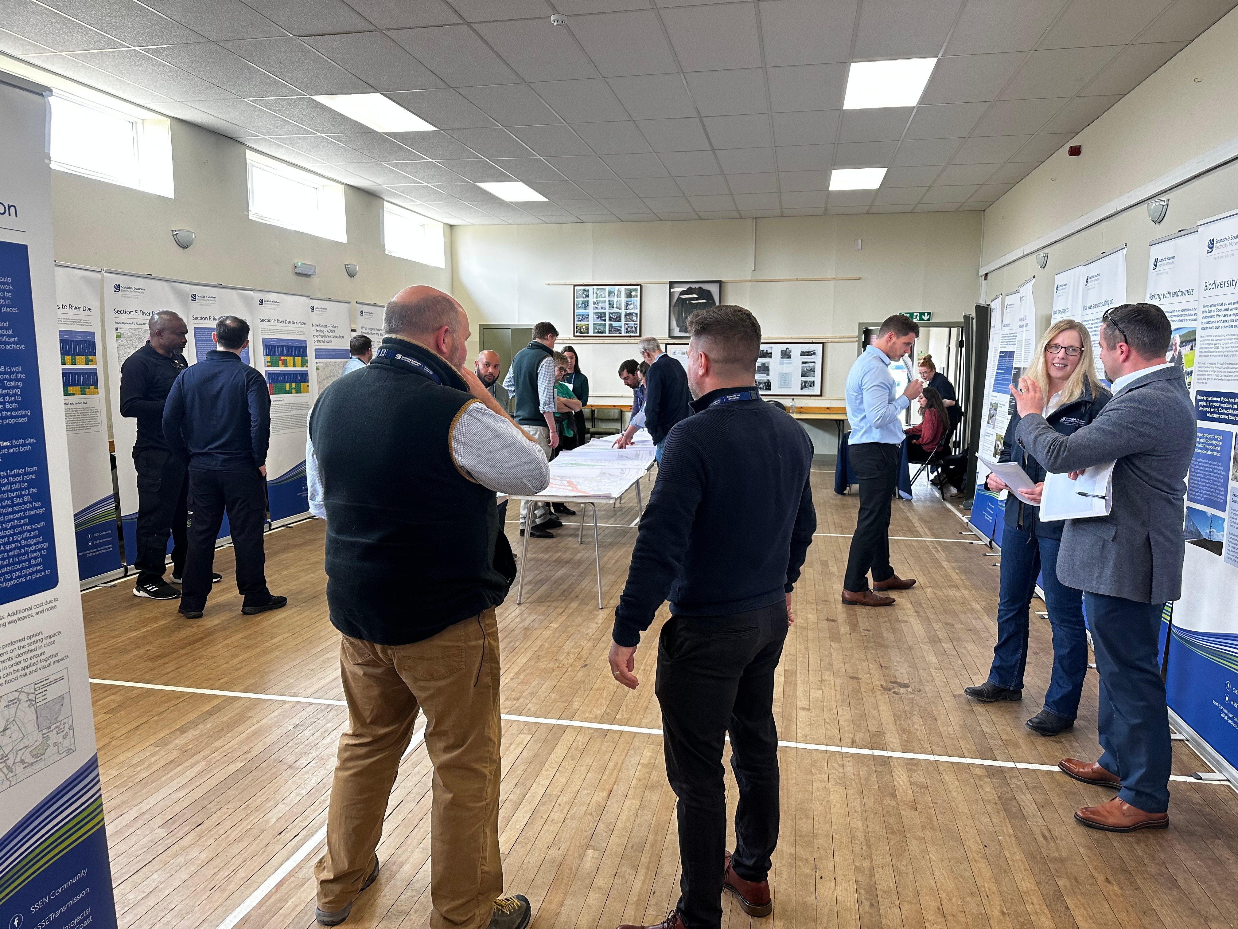 Members of the public and SSEN Transmission employees examining project posters in a hall.