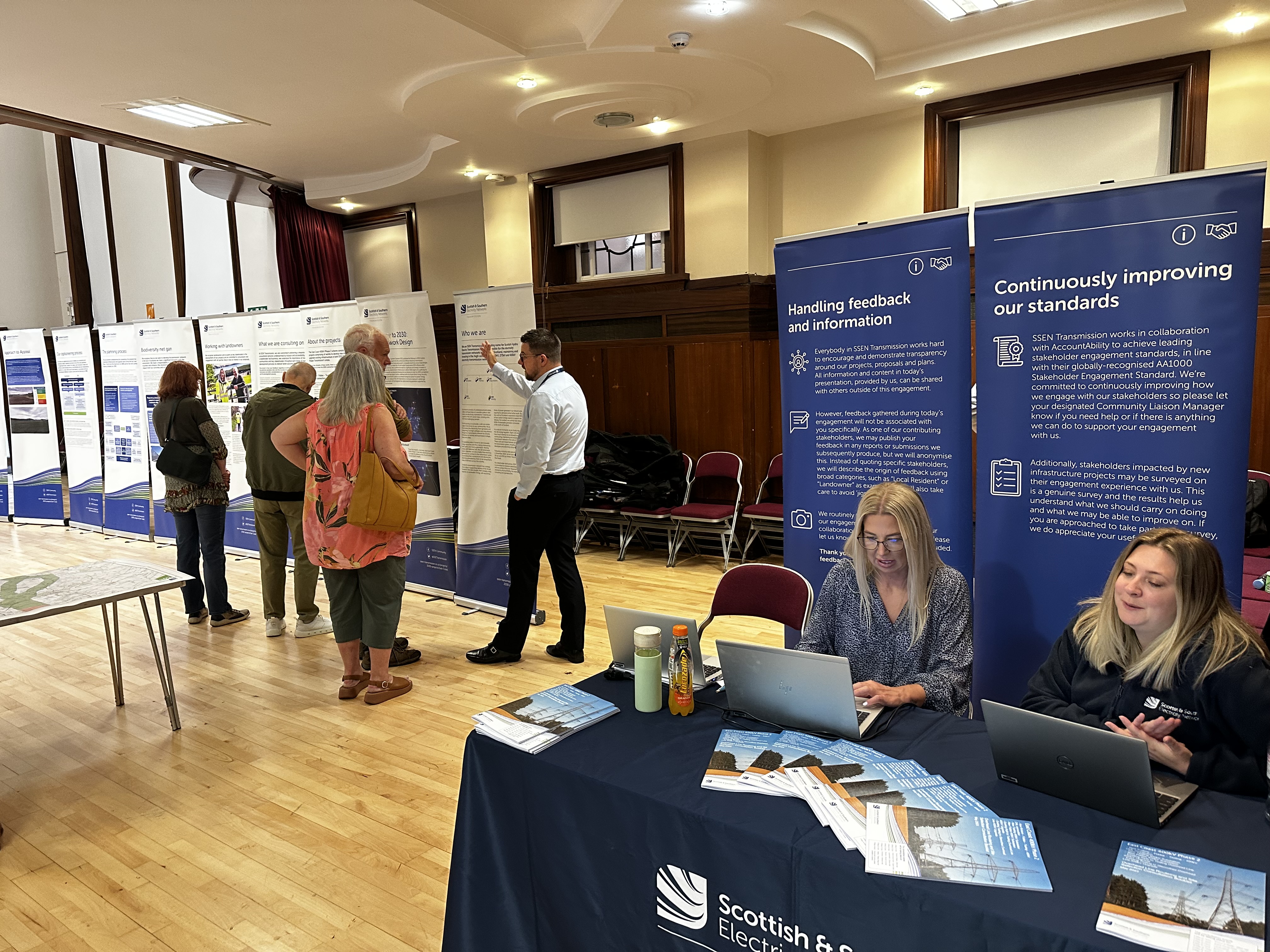 Members of the public and SSEN Transmission employees examining project posters in a hall.