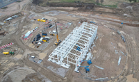 An aerial view of a construction site. A white metal framed building under construction is prominent.