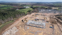 A metal framed building under construction on a construction site. A substation is visible nearby.