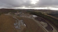 An aerial view of a substation under construction, close to the viewpoint is a metal transmission tower base, other transmission tower parts lie nearby.