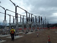 Substation infrastructure in a substation under construction, a contractor in PPE and a harness stands nearby.