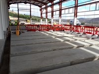 View from inside a metal frame building on a construction site. Concrete cuboids line the floor in rows.