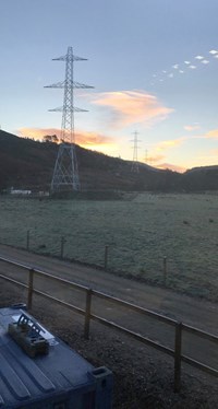 Metal transmission towers in front of a sunset.
