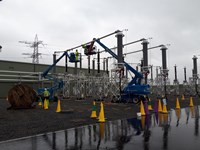 Contractors atop mobile elevated platforms amongst substation infrastructure.