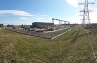 A wide view of a fenced substation, inlcuding several green buildings and a various kinds of substation infrastructure.