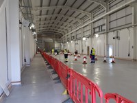 Several contractors in PPE standing in a metal framed building. There are several cones and construction barriers and one contractor in the background holds a power-washer.