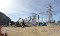 Contractors directing construction vehicles on a construction site, surrounded by substation infrastructure.