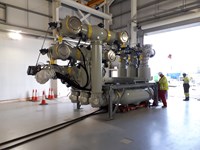 A section of transmission infrastructure resting on the floor of a metal-framed building. A contractor interacts with the far-right corner of the device.