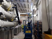 A section of substation infrastructure within a metal-framed building. A contractor in PPE stands on a mobile raised platform and others look up from below.