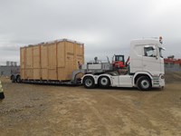 A large, rectangular wooden box on a flat-bed trailer attached to a lorry.