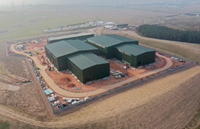 An aerial view of a construction site. Large, green, metal walled buildings are present on site.