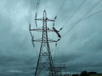 Contractors in PPE atop a metal transmission tower, a gantry is suspended from one arm.