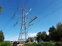 A contractor in PPE atop a gantry suspended from a metal transmission tower.