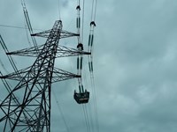 A view from below a metal transmission tower. Contractors in PPE sit atop the transmission lines themselves.