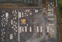 An overhead view of a construction site,  there are several large indendations within the ground filled with concrete, and some have concrete blocks within them. Several construction vehicles are present at various locations.