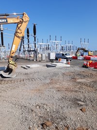 Concrete cubes imbedded in rough ground, the arm of a digging attachment is visible and there is substation infrastucture in the background.