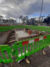 A concrete structure embedded within the ground on a construction site, substation infrastructure is visible in the background.