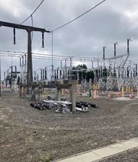 A concrete and metal structure, the metal components lay separately on the ground. Newer substation infrastructure is visible in the background.