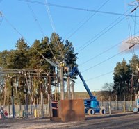 A contractor in PPE on a mobile platform interacting with substation infrastructure.