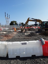 An excavator and contractor in PPE standing next to a trench in a substation under construction.