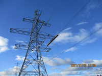 A contractor in PPE atop a metal transmission tower. A date reads "2021/11/03 12:00".