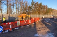 A contractor in PPE and an excavator in a fenced-off area.