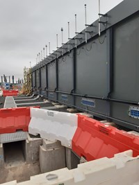 A row of antennas fixed to a metal wall above a series of concrete trenches.