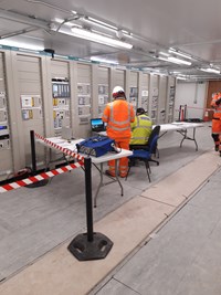 Contractors in PPE sat with a laptop next to a bank of machines.