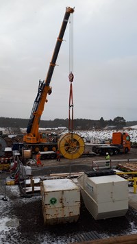 A Large steel cylinder suspended by chains from a crane on a construction site.