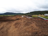 A dirt area covered with tire tracks. Black and green cylinders lay to one side.