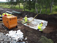 Contractors in PPE in an excavated area. Construction materials lay nearby.