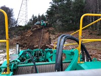 View from a construction vehicle up a dirt hill towards another construction vehicle.