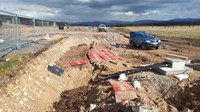 An excavated area of a construction site, covered with red slabs, black cables emerge from the ground.