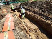 Contractors in PPE in a trench operating construction machines.