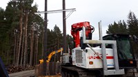 A construction vehicle in front of a trident woodpole tower.