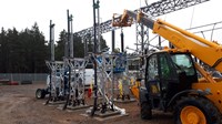 A contractor in PPE atop substation intrastructure, a section is suspended from the arm of a construction vehicle.