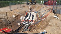 A series of different colour and sized tubes across the bottom of an excavated area.