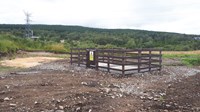 A wooden fenced area with an "Underground Live Cables" label on the gate. Within the area are two concrete sections surrounded by gravel.