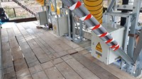 Three white metal boxes with high voltage warnings, amongst metal structural supports in a wood-floored area.