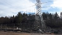 Contractors in PPE atop a scaffolding structure next to a metal transmission tower.