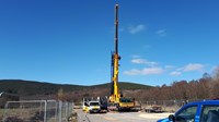 A large crane vehicle on a construction site, several large cable drums are visible behind the crane.