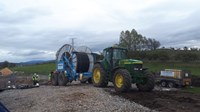 A tractor attached to a trailer containing a large cable drum on a construction site.