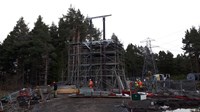 Contractors in PPE below a trident woodpole tower surrounded by scaffolding.