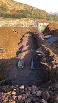 Green and black cylinders semi-buried in a trench on a construction site.